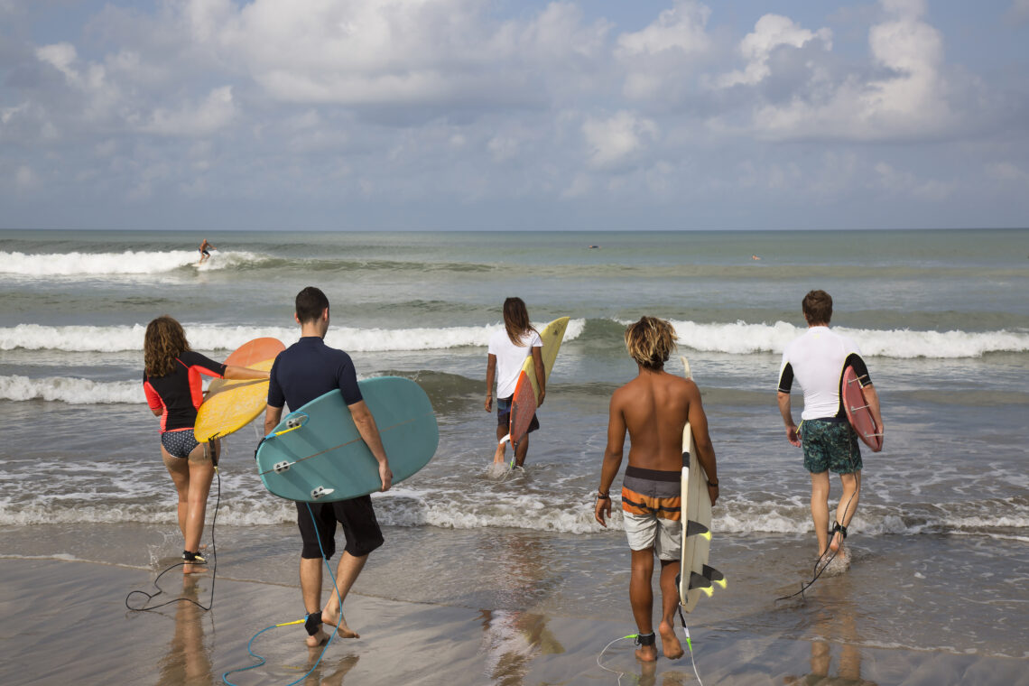 Fünf Surfer gehen ins Meer um auf die perfekte Welle zu warten